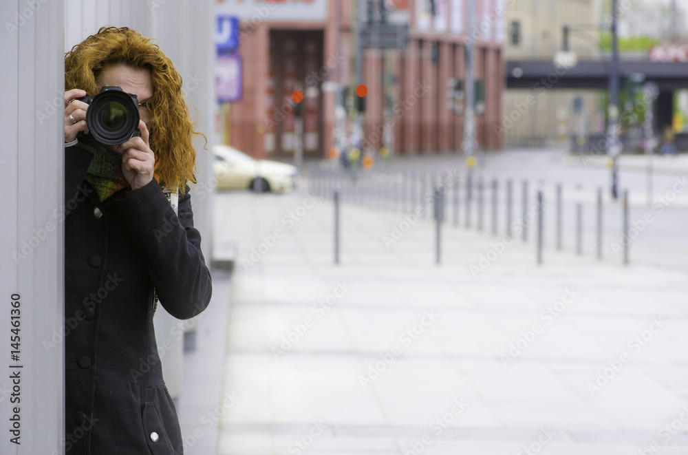 Fototapeta premium Eine Fotografin steht hinter einem Pfeiler eines Gebäudes und fotografiert heimlich