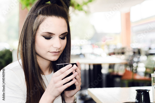 portrait of a beautiful young woman in a cafe with a cup of coffee in her hands  close-up