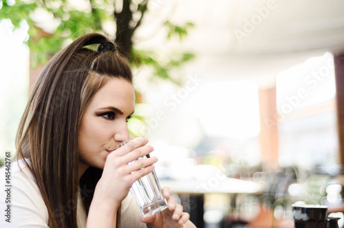 beautiful young girl or woman sitting in a cafe and drinking a glass of water, summer days and hydration