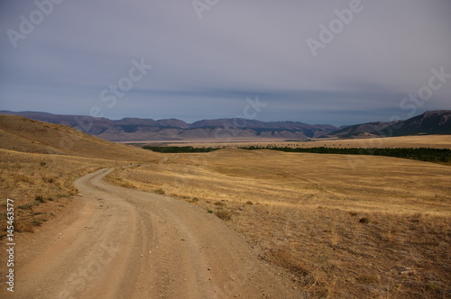 Road through a dry desert steppe on a highland mountain plateau with yellow grass with ranges on a horizon  Kurai  Altai  Siberia  Russia