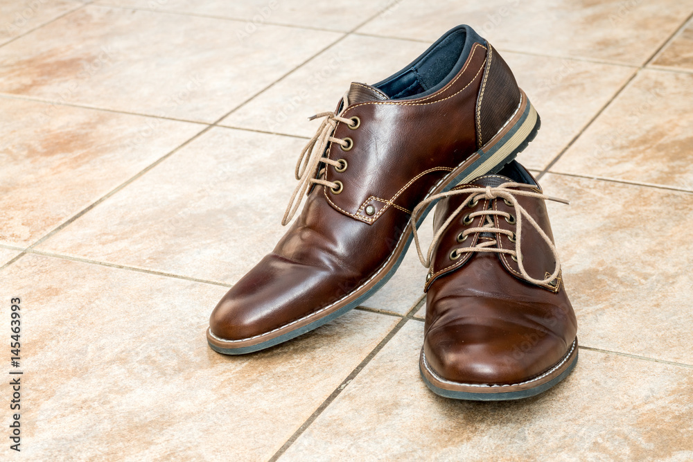 Pair of fashion brown men's shoes with shoestring on a light brown ceramic tiles Pair of fashion brown men's shoes with shoestring on a light brown ceramic tiles