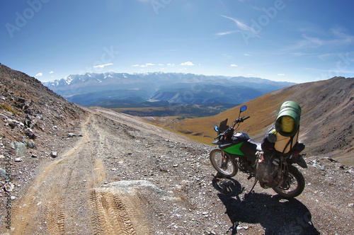 Motorcycle enduro traveler standing on high mountain stone road fish-eye view with snow on the background of snowy peaks Altai Mountains, Siberia, Russia