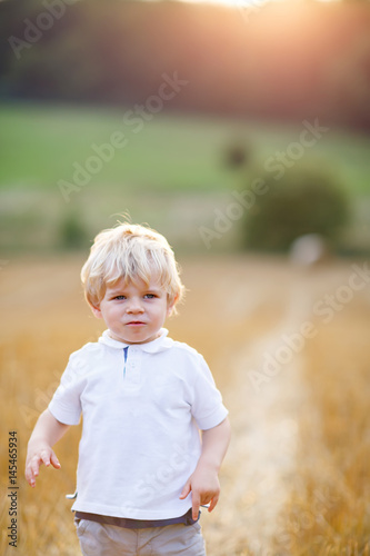 Happy blond kid boy enjoying sunset in wheat field.