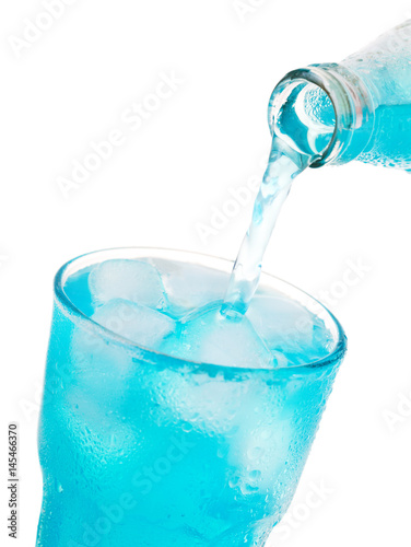 pouring blue soda into glass with ice from bottle