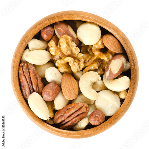 Raw mixed nuts in wooden bowl. Dried walnuts, hazelnuts, almonds, cashews, macadamia, Brazil and pecan nuts. Fancy mix of snack food. Isolated macro food photo close up from above on white background.