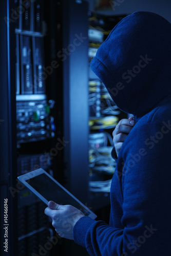 Hooded computer hacker stealing information with Tablet PC