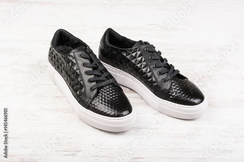 Pair of black ladies' sport leather shoes on white wooden background.