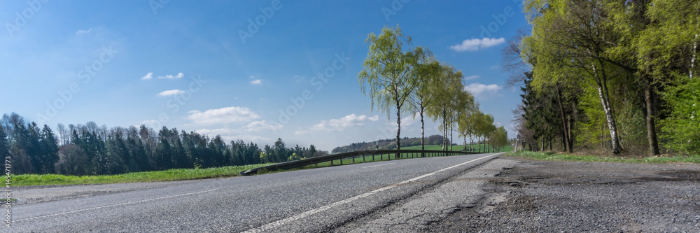 Landstraße mit Straßenschäden bei blauem Himmel und Sonnenschein, bodennahe Sicht