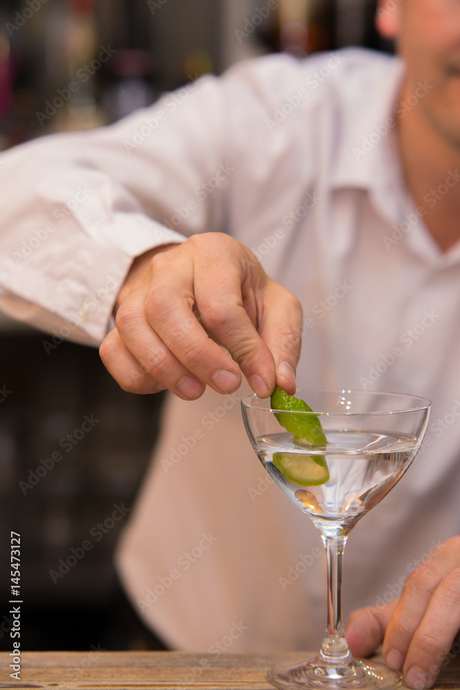 Closeup of barman hand putting lemon peel on a glass to prepare cocktail.