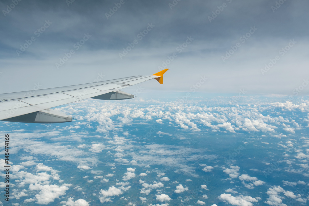 Fototapeta premium Wing of an airplane flying above the clouds see through the window. Business concept.