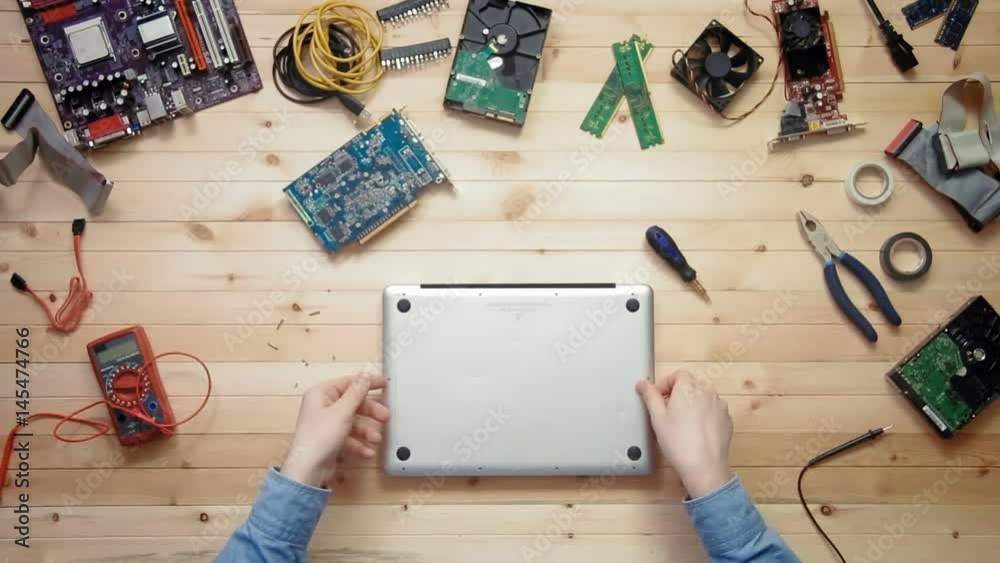 Top view computer technician opens broken laptop computer and repairs it at wooden desk with tools and electronic components