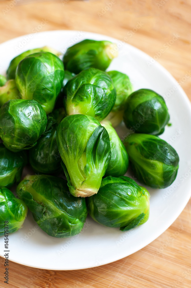 Pile of Fresh Green Brussels sprouts on a white plate on wooden table with copy space, close up Pile of Fresh Green Brussels sprouts on a white plate on wooden table with copy space, close up