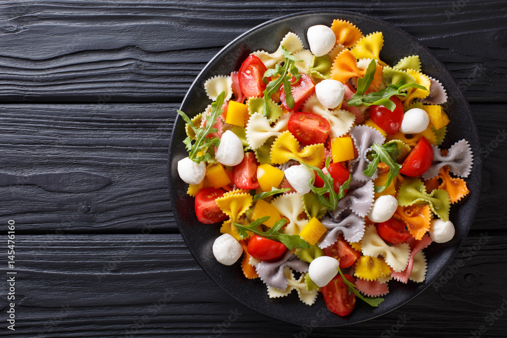 Warm salad of farfalle pasta, tomatoes, arugula and mozzarella closeup. horizontal top view