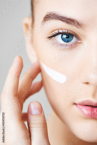 A young girl on a white background apply moisturizer on face closeup