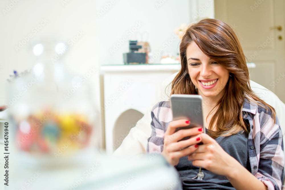 Smiling young woman using mobile phone at home. Smiling young woman using mobile phone at home.