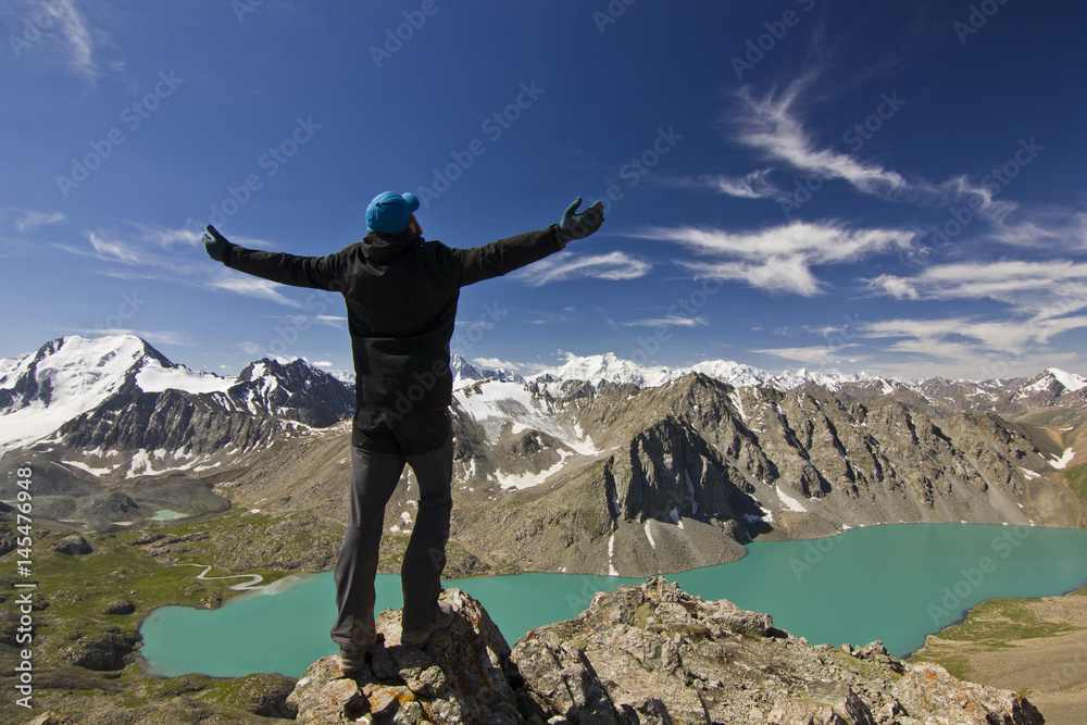 man in black jacket standing with hands-up above blue lake in mountains man in black jacket standing with hands-up above blue lake in mountains
