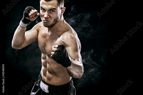 Sportsman muay thai boxer fighting in boxing cage. Isolated on black background with smoke. Copy Space.