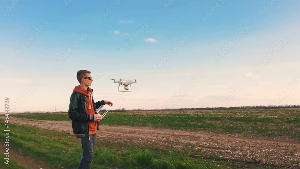 Quadrocopter drone takes off from the pilot's hand and hovers over the guy at sunset. The guy starts a drone on a green glade against the backdrop of a green field. Slow motion (90 fps). Quadrocopter drone takes off from the pilot's hand and hovers over the guy at sunset. The guy starts a drone on a green glade against the backdrop of a green field. Slow motion (90 fps).