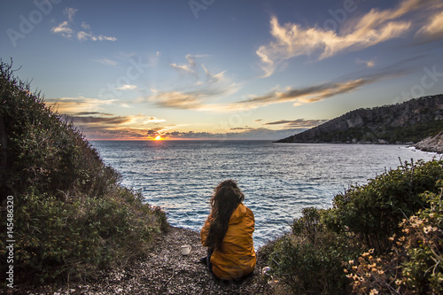 girl in yellow jacket sitting near seashore at sunset