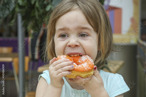 A small child bites a sweet donut. A child is a girl 4-5 years old.