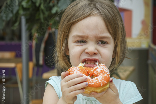 A small child bites a sweet donut. A child is a girl 4-5 years old.