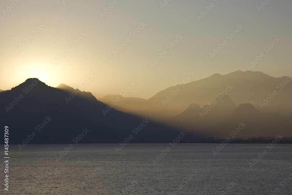 yellow sunset above sea with mountains on background