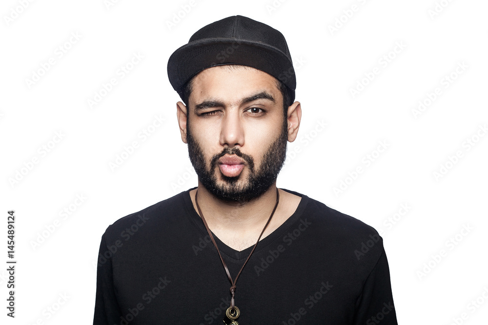Portrait of young man with black t-shirt and cap looking at camera with wink and kiss. studio shot, isolated on white background. Portrait of young man with black t-shirt and cap looking at camera with wink and kiss. studio shot, isolated on white background.