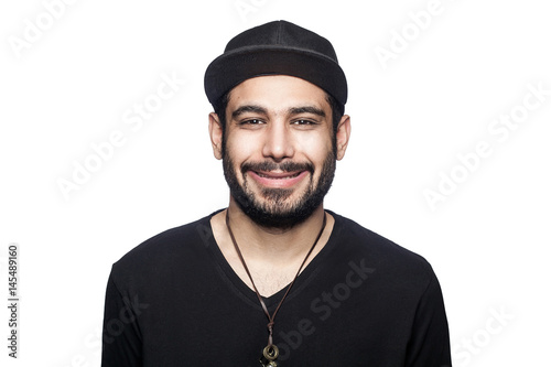 Portrait of young happy smilely man with black t-shirt and cap looking at camera with toothy smile. studio shot, isolated on white background.