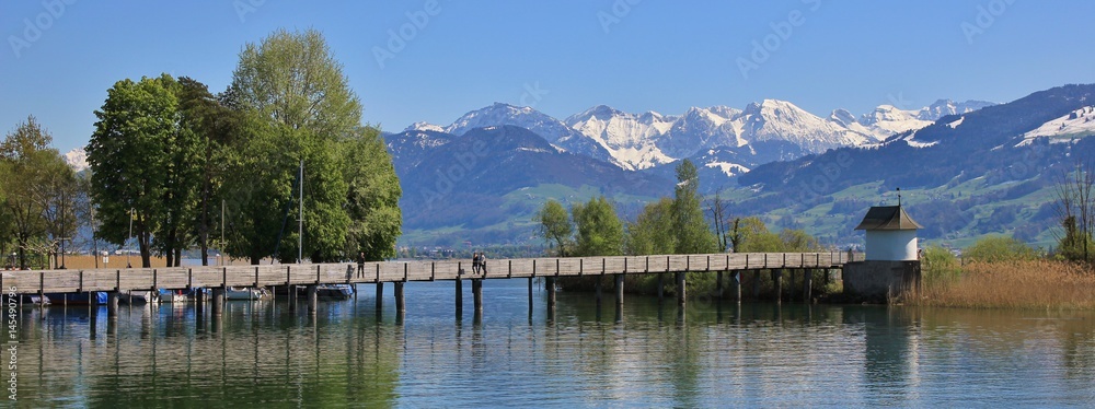 Naklejka premium Timber gangplank in Rapperswil. Lake Zurichsee and snow capped mountains. Springtime.