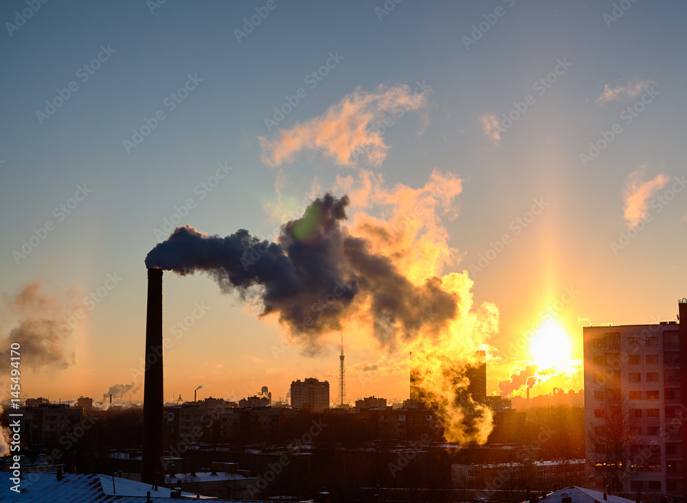 Smoke from industrial chimneys at sunset over the metropolis. A solar halo, a rainbow and snow. St. Petersburg.