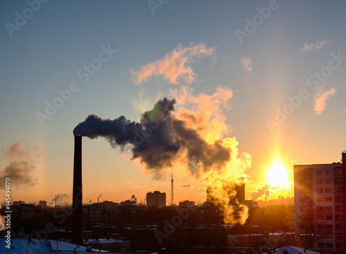 Smoke from industrial chimneys at sunset over the metropolis. A solar halo, a rainbow and snow. St. Petersburg.