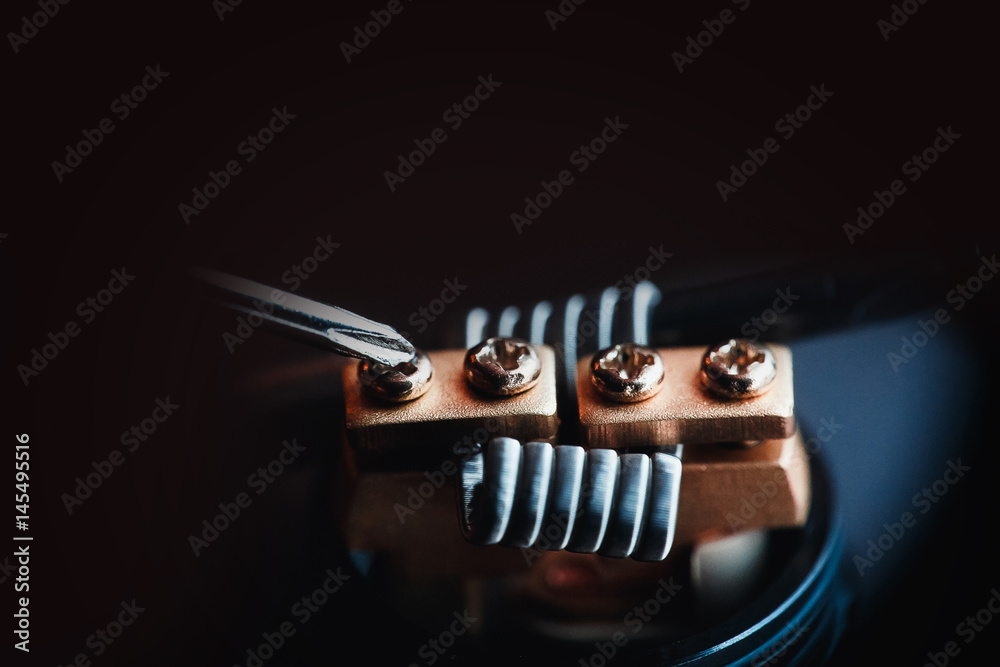 Vape,electronic cigarette over a dark background. screwdriver spins the bolts on the coils. Vape,electronic cigarette over a dark background. screwdriver spins the bolts on the coils.