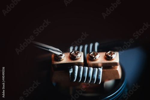 Vape,electronic cigarette over a dark background. screwdriver spins the bolts on the coils.