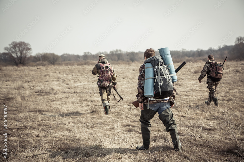 Hunting scene with group of hunters with backpacks and hunting ammunition going through rural field during hunting season in overcast day Hunting scene with group of hunters with backpacks and hunting ammunition going through rural field during hunting season in overcast day