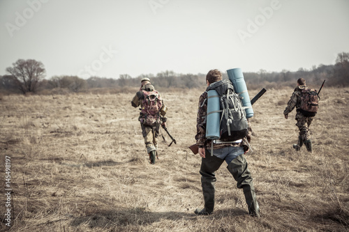 Hunting scene with group of hunters with backpacks and hunting ammunition going through rural field during hunting season in overcast day
