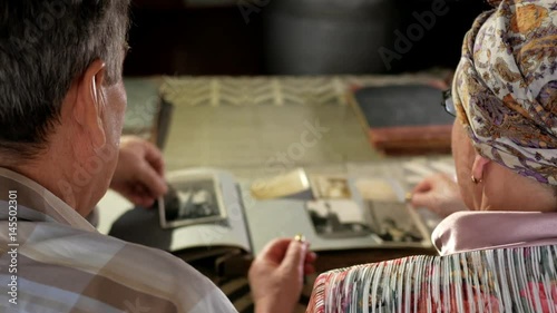 An elderly couple man and woman are looking at their old photos at home and talking. A man with a mustache, a wife with glasses