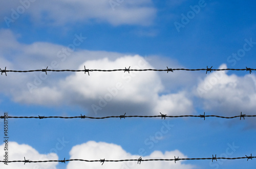 Blue sky with white clouds behind wire mesh. 
