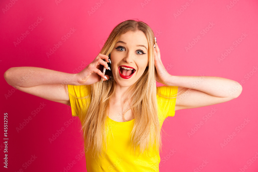 excited blonde teenage girl talking on smart phone over pink background excited blonde teenage girl talking on smart phone over pink background