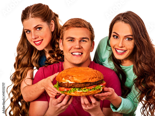 Hamburger fast food with ham in people hands . Fast food concept. Friends man and two women eating sandwich junk in party. Girls fool around and feed man.