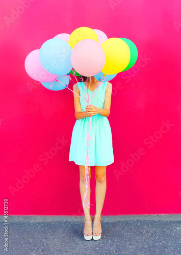 Happy woman is hides her head an air colorful balloons having fun over pink background