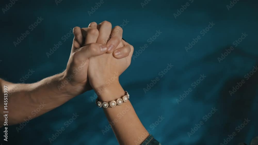Loving heterosexual couple passionate interlock fingers woman in denim shirt with bracelet on wrist and black nail polish on blue background close up