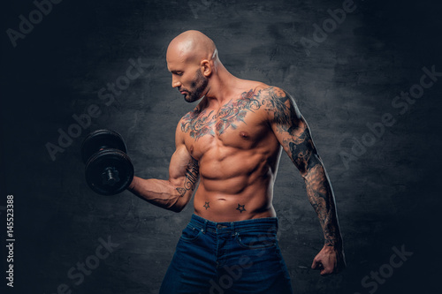 Positive shaved head shirtless male dressed in a jeans holds the dumbbell. © Fxquadro