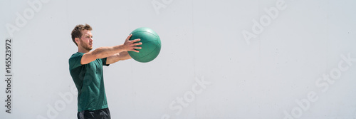 Banner. Medicine ball gym workout fitness man strength training arms doing front raise exercise for shoulder muscles. Upper body weighted ball workout at fitness centre. Panorama crop with copy space.