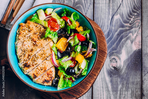 Greek salad and roasted chicken in plate on wooden table background. Top view with copy space. Healthy food