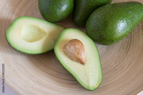 Avocado halves with seed in a wood plate on a white colored background