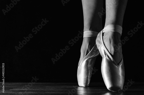 Close-up classic ballerina's legs in pointes on the black floor