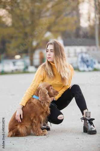 Portrait. A beautiful sexy girl, blonde, a young woman looking like Jennifer Aniston is siting with a Cocker Spaniel dog, against a backdrop of urban homes in a sleeping area. photo