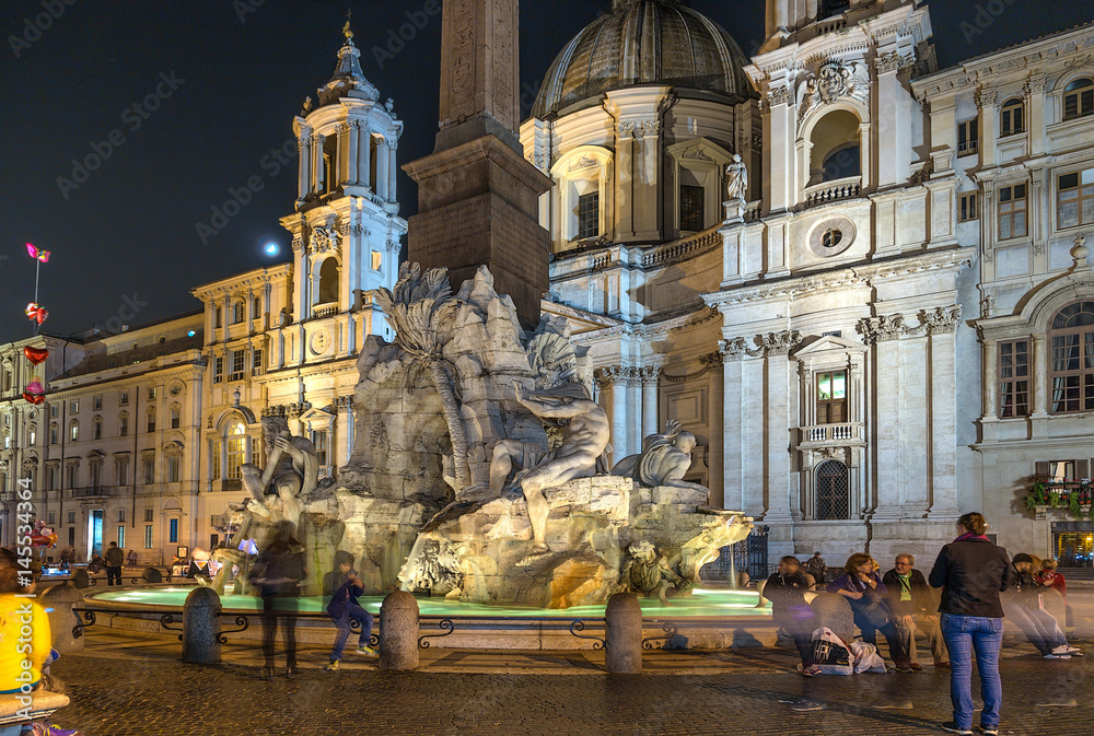 Rome, Italy. Tourists at the fountain of the Four Rivers (1651) in Navona Square against the backdrop of the Church of Sant'Agnese in Agone (1652). Night, backlight