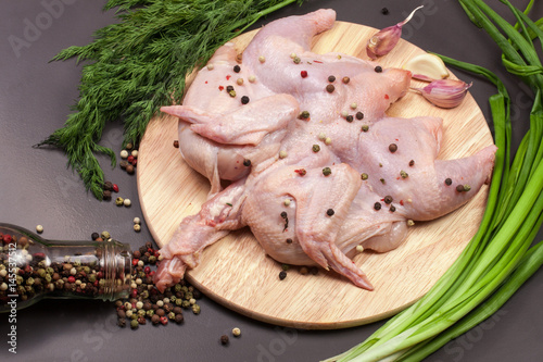 raw chicken carcass with peppercorns and greenery on the cutting board on a dark background