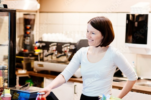 Satisfied female owner of a local store stands smiling behind the counter
